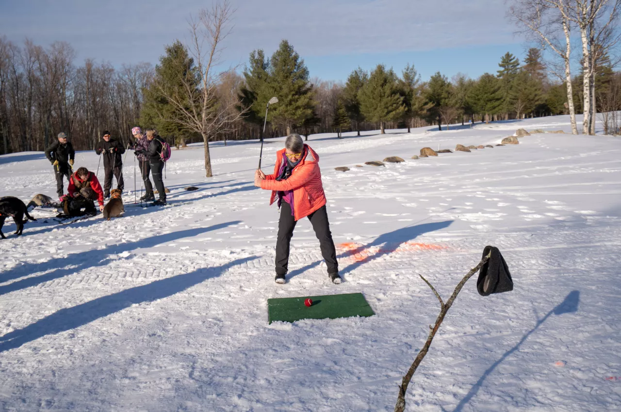 An adult prepares to tee off on a small square of artificial grass on a snowy field.