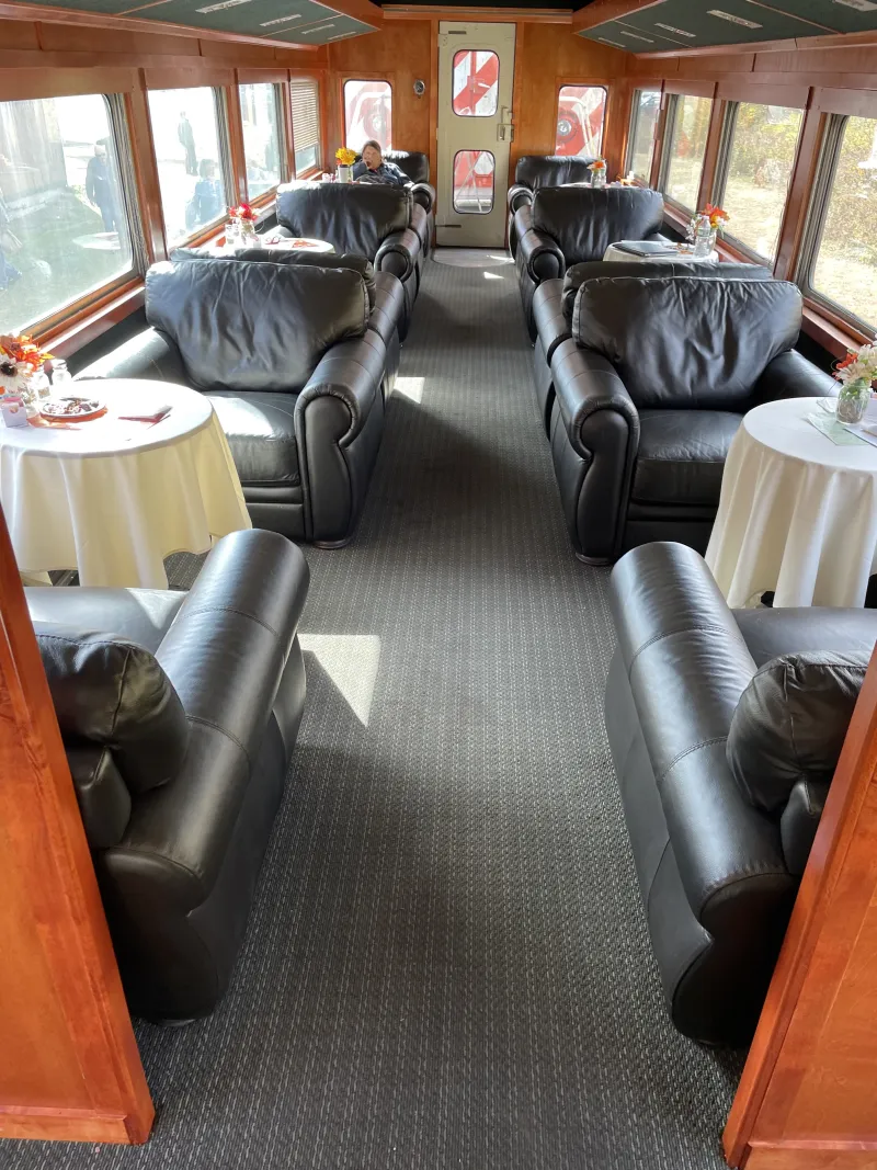 Large, comfy leather chairs sit in pairs at small tables in a passenger rail car.