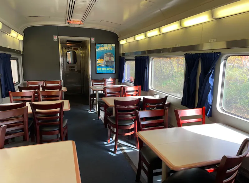 Square tables surrounded by four chairs at each table on either side of the aisle on a railcar.