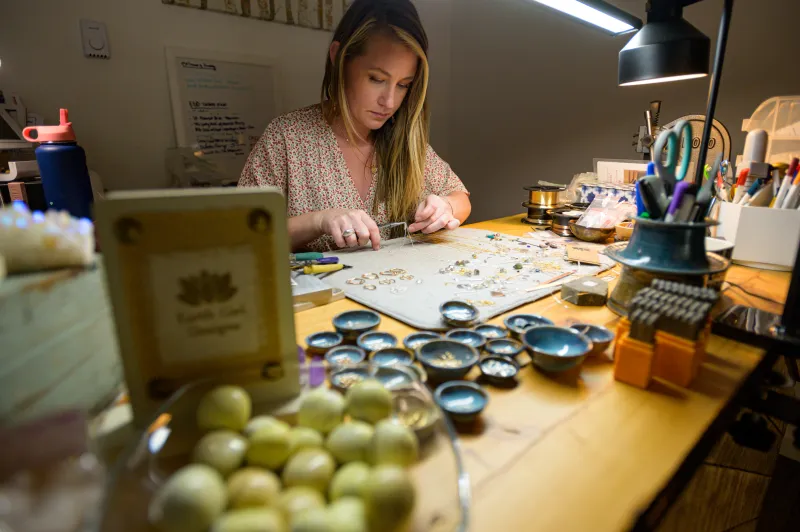 A woman mends handmade jewelry at a work bench,
