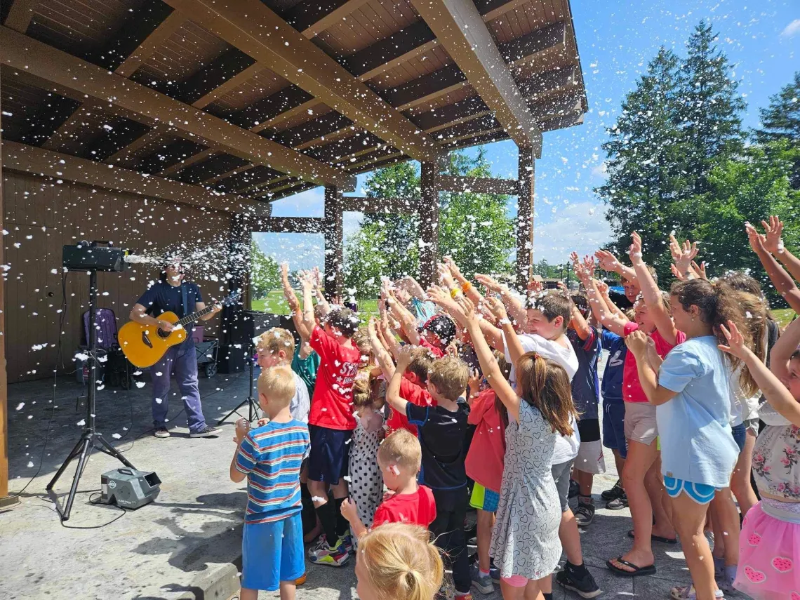 Kids wave their hands in bubbles at a band shell performance.