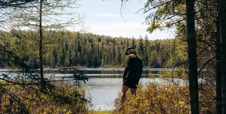 A hiker stands at the edge of an opening to a pond