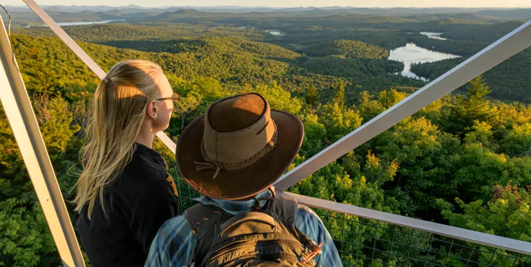 Two people look at the view from a spot on the stairs up a firetower