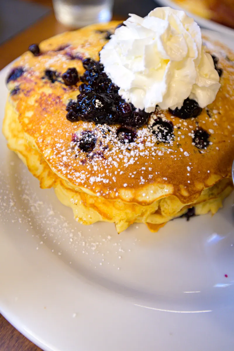 a stack of three blueberry pancakes with whipped cream on top.