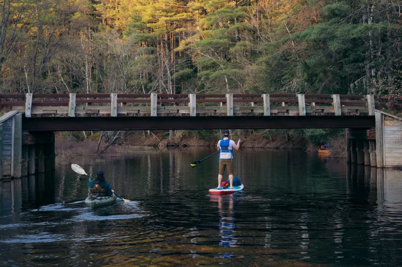 A kayaker and a stand up paddleboarder approach a bridge