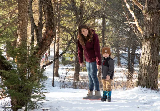 A mother and son pose for a picture in snowy woods.