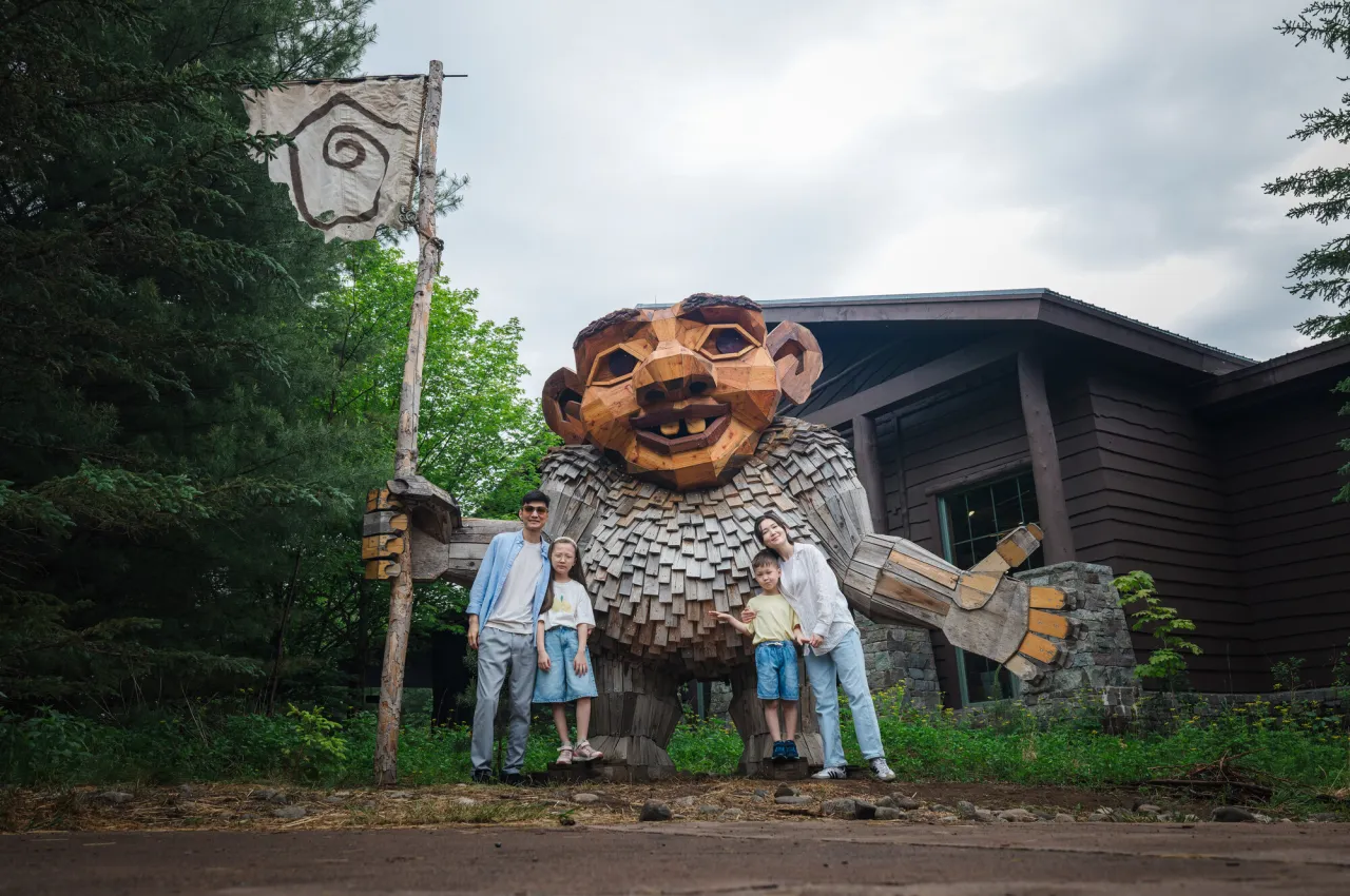 A family of two adults and two children pose for a photo with a giant wooden troll.