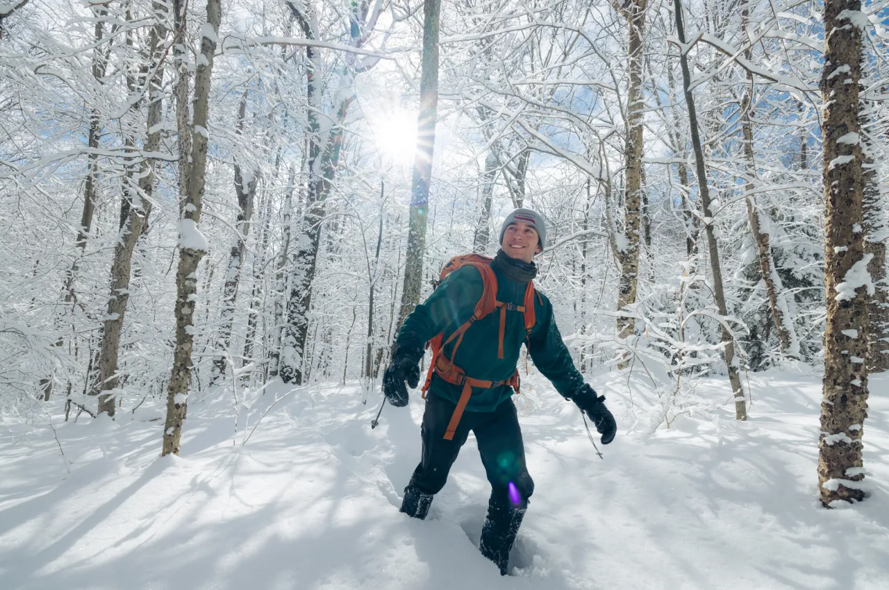 A hiker smiles amid a snowy forest while hiking a trail.