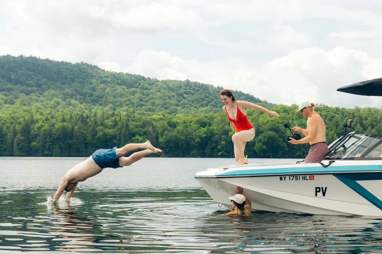 A man and woman jump off a boat into a lake.