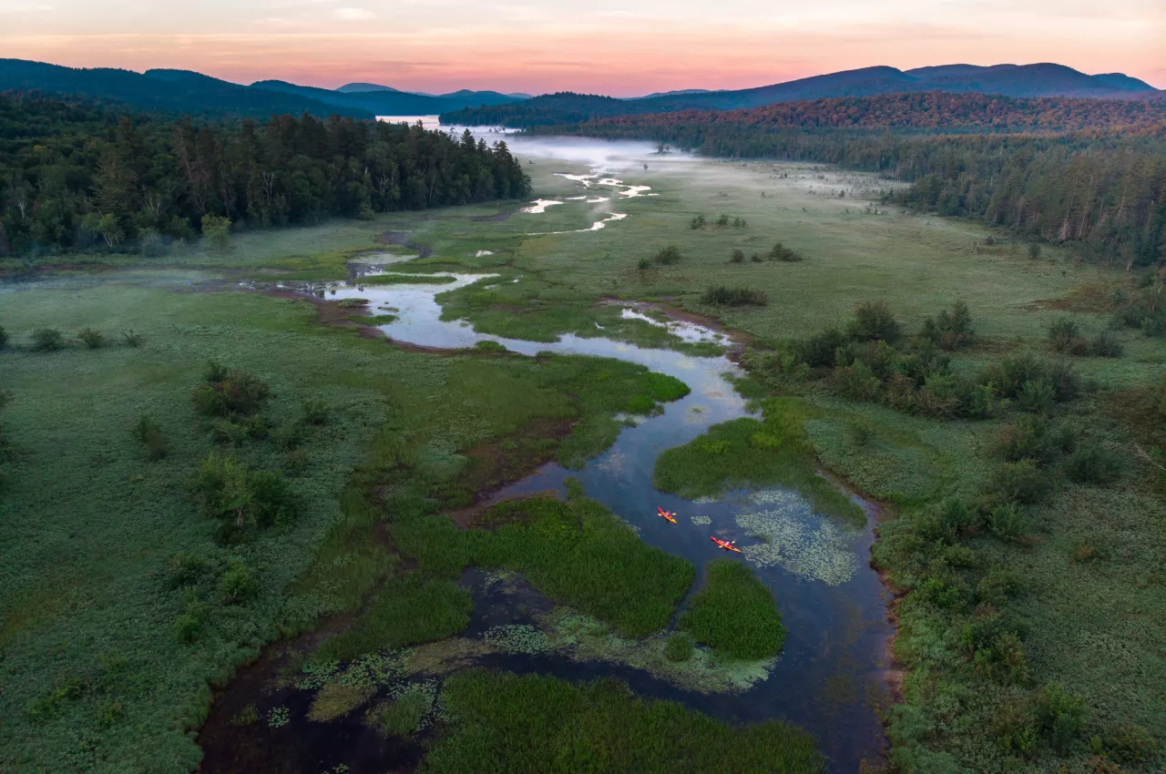 An aerial view of one of the winding rivers in the Tupper Lake region surrounded by a mountainous landscape