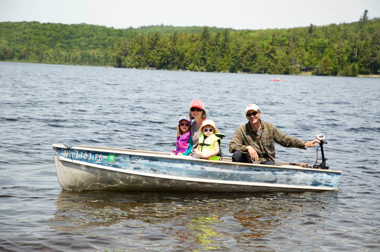 A family of four smiles as they ride in a motorboat on an Adirondack lake
