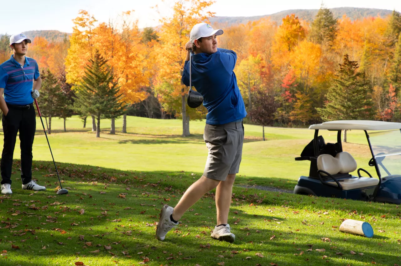 Golfer tees off on a beautiful fall day while his friend waits his turn