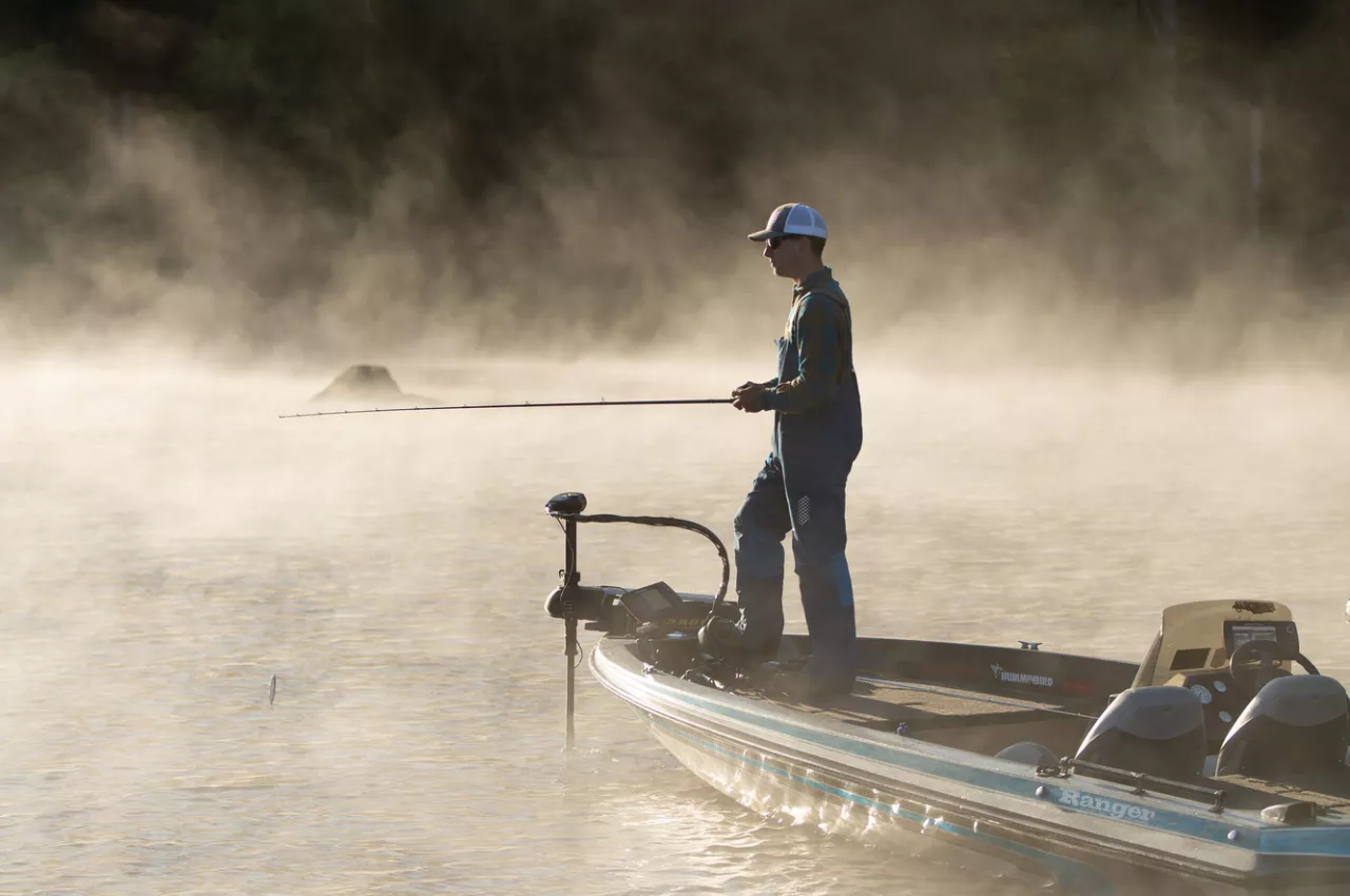 An angler casts his line from the front of a fishing boat on a foggy spring morning.