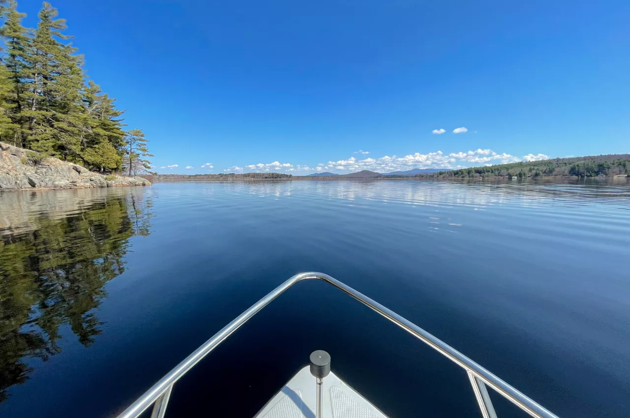 A blue lake under a nearly cloudless sky, as viewed from the bow of a small metal boat.