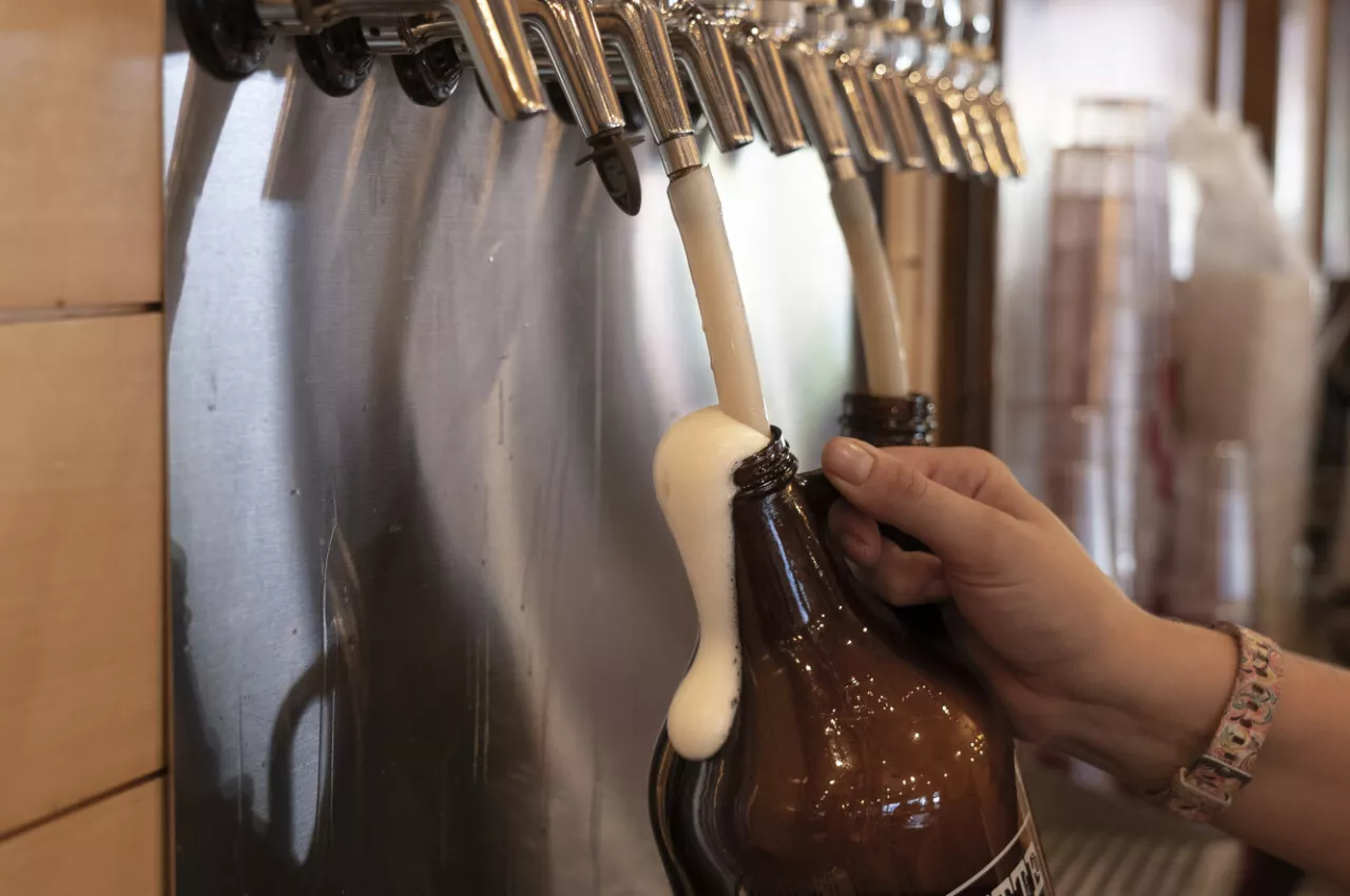 A person fills up a growler of beer from the tap. 