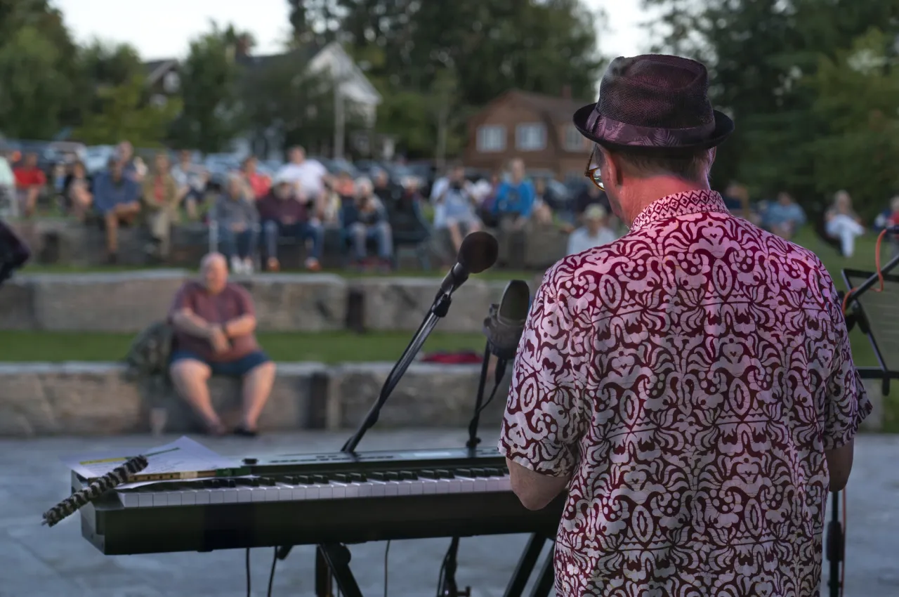 A man playing an electric keyboard in front of rows of people at an outdoor park. 