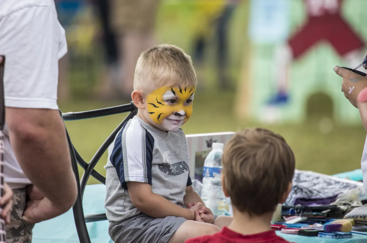 A small child smiles under a coating of face paint at a carnival.