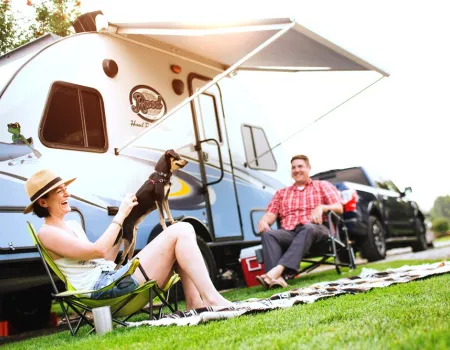 People smile and laugh in lawn chairs under the awning of their camper