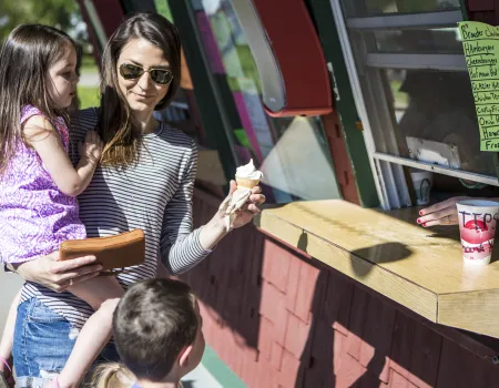 A mom holds her kid in one hand and an ice cream cone in the other.