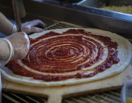 pizza dough with tomato sauce being spread on it