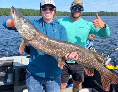 Two people holding a giant pike while giving thumbs up.