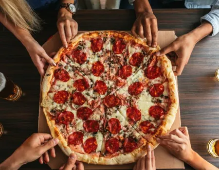 Lots of hands reach to pull a slice of pizza