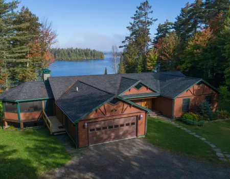An aerial view of a cabin by a lake surrounded by tall pines.