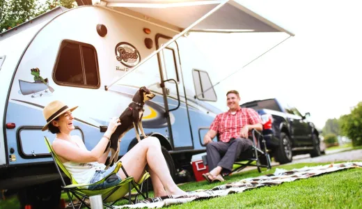 People smile and laugh in lawn chairs under the awning of their camper
