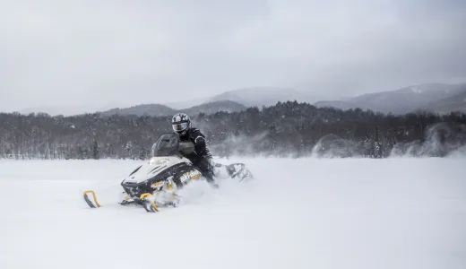 A person on a black and yellow snow machine in a field.