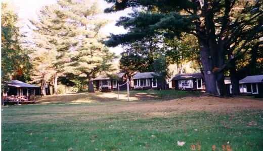 A brown house with white trim tucked in the pine forrest beyond a large lawn.