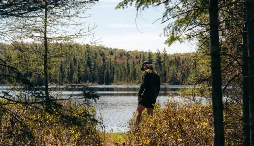 A hiker stands at the edge of an opening to a pond