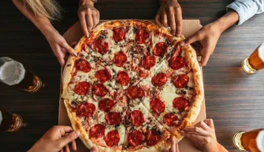 Lots of hands reach to pull a slice of pizza