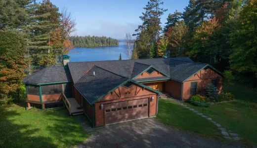 An aerial view of a cabin by a lake surrounded by tall pines.