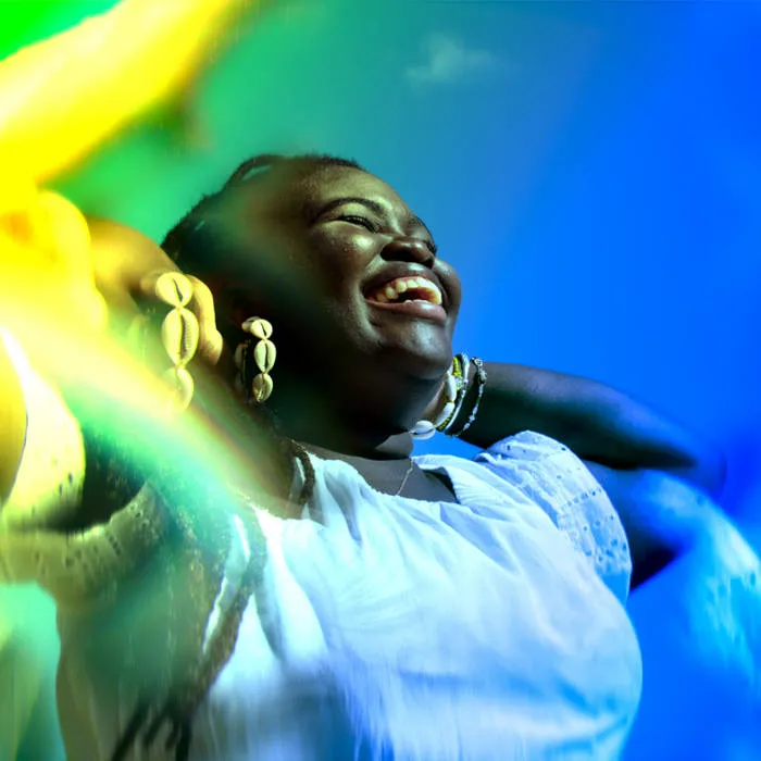 A colorful, blue and yellow-hued photo close-up of a smiling Black woman with long hair.