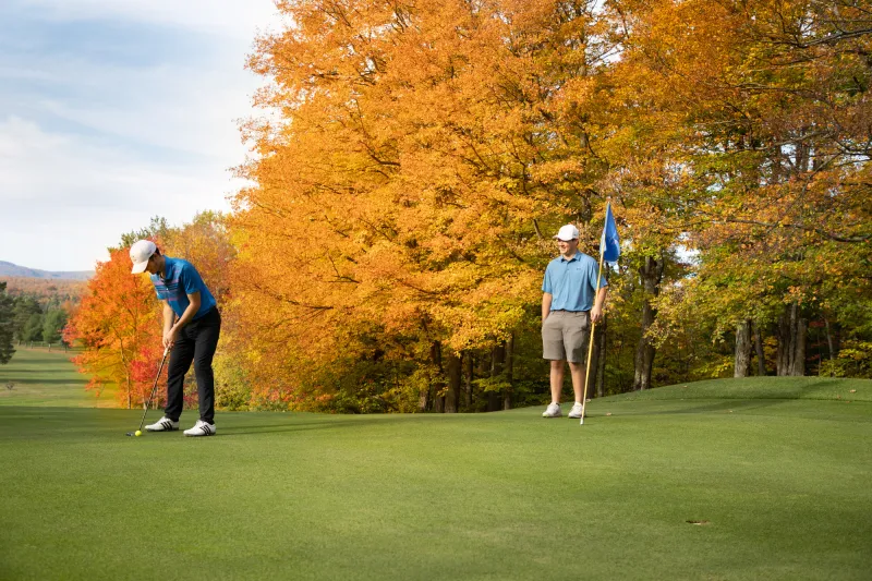A man sets up his swing on a golf course in fall.