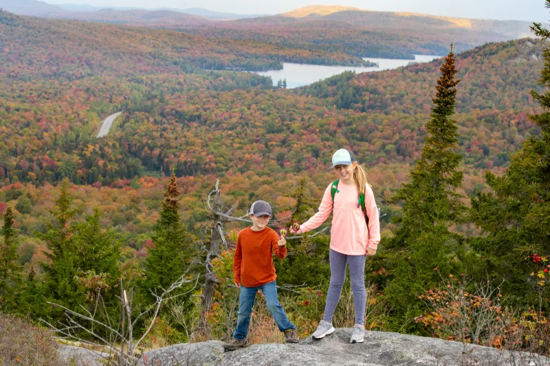 A young girl and boy stand at the top of a mountain in fall.