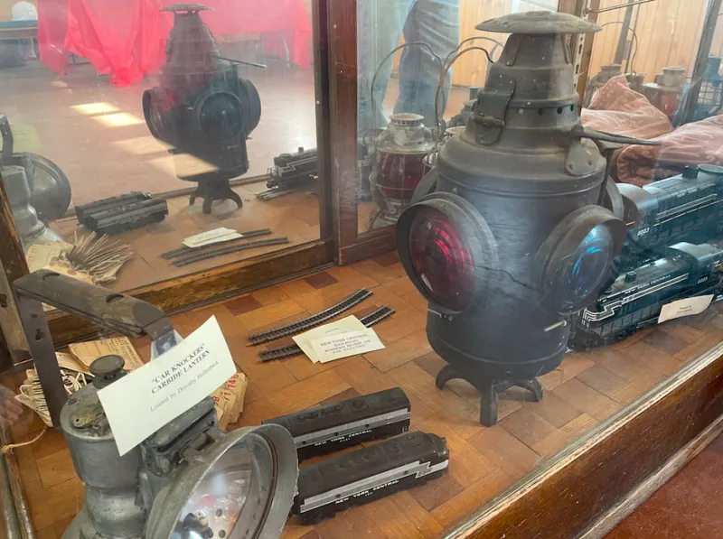 A glass display case holds railroad antiques, including a metal and glass lantern.