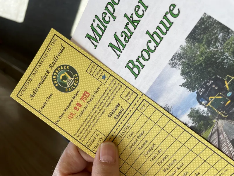 An old-fashioned style train ticket next to a train ride brochure.