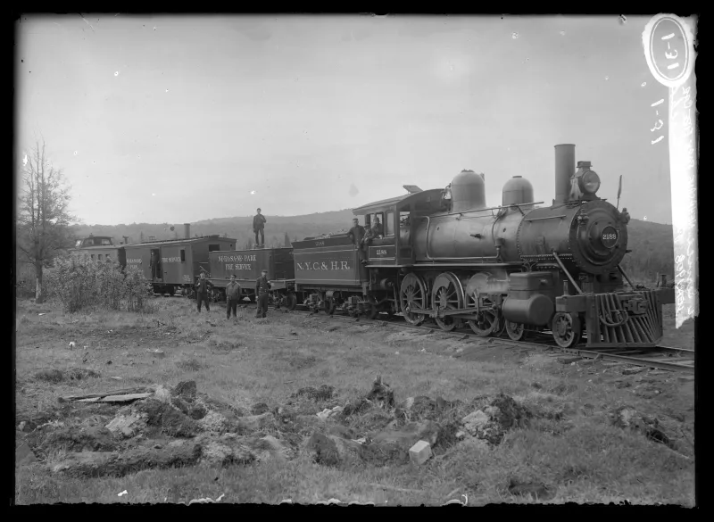 A black and white, vintage image of a fire service train with steam locomotive and coal car stopped on tracks.