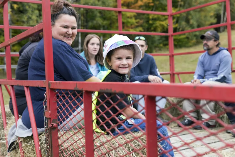 A young boy smiles from his perch on a hay bale on a red wagon hay ride.