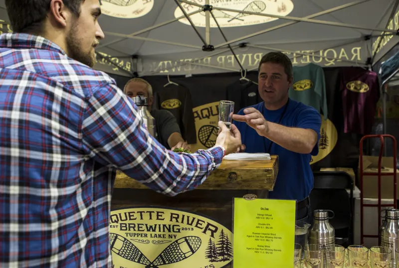 A man at a beer tent hands a glass of beer to a customer.