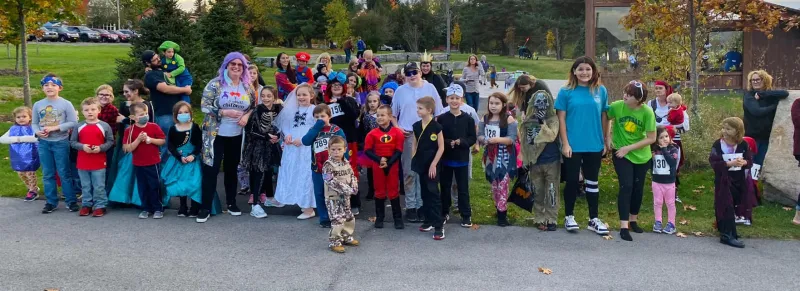 An array of children, many in Halloween attire, smile for the camera as a group before a fun run.