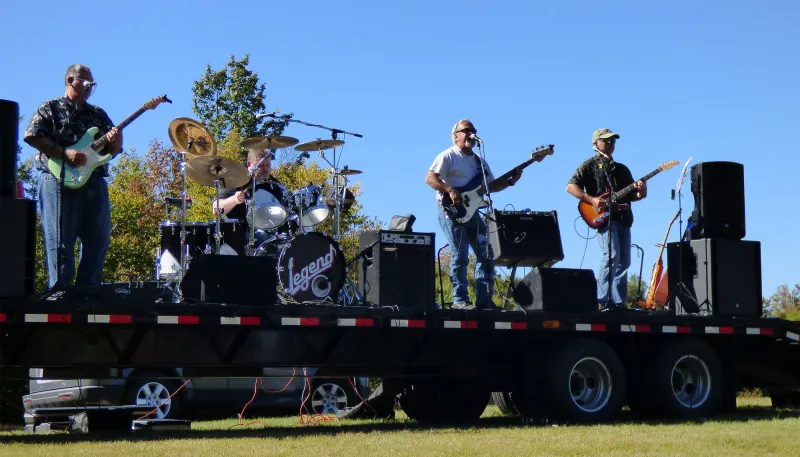 A music group performs on a flat stage in front of a blue sky.