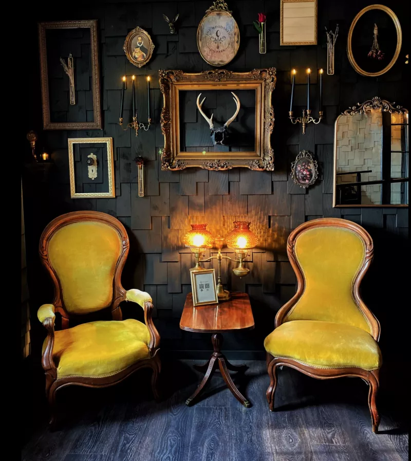 entryway to the restaurant with yellow upholstered chairs and a charming backdrop of gold vintage frames and rustic decor like antlers