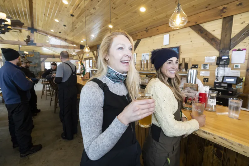 A woman in snow gear laughs with a drink in her hand while at a brewery.
