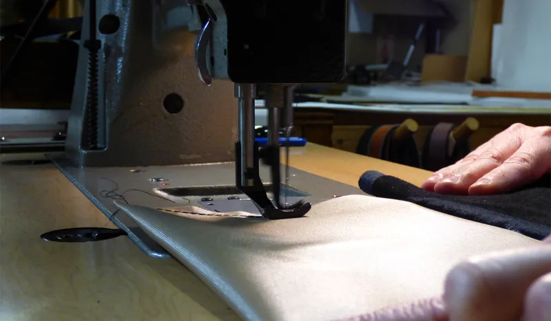 Artisans stitch the ripstop fabric lining for a leather handbag.