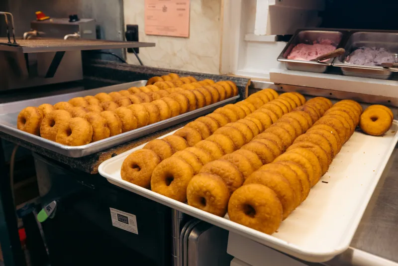 Freshly deep-fried donuts cool on trays in a donut shop kitchen.