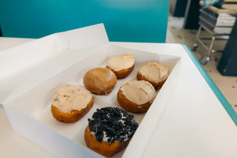 A box of six donuts, each with different frosting on top, sits on a booth table.