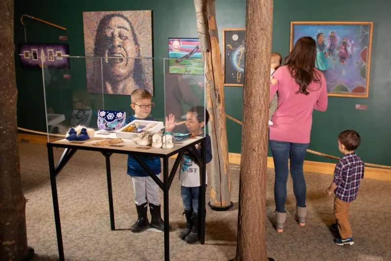 Adults and children explore a portion of a museum exhibit on indigenous culture.