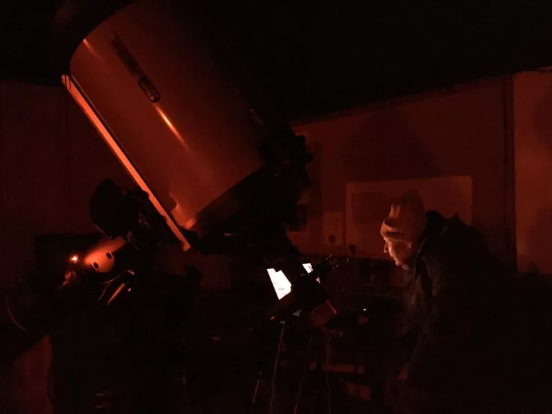 George Normandin controls a 14" Celestron with a laptop in red light conditions.